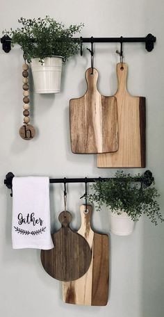 three wooden cutting boards hanging on a wall with plants and potted plants next to them