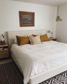 a bed with white sheets and pillows in a bedroom next to a painting on the wall