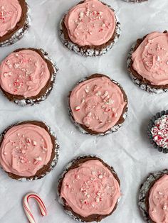 chocolate cookies with pink frosting and candy canes on top, next to peppermint candies