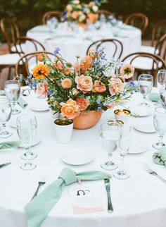 an arrangement of flowers in a pot on top of a table with place settings and napkins