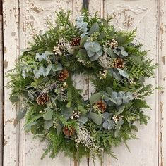 a wreath hanging on the side of a door with pine cones and greenery around it