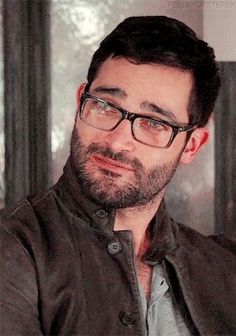 a man with glasses and a beard wearing a leather jacket is looking at the camera