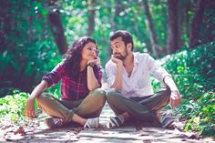 a man and woman sitting on the ground in front of trees, one is holding her mouth