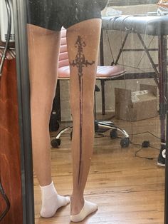 a person standing in front of a mirror with a cross tattoo on their leg and legs