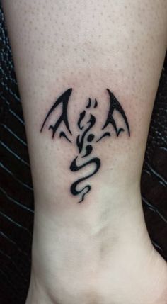 a small tattoo on the foot of a woman with a dragon design in black ink