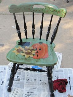 a green wooden chair with painted pumpkins on it's seat and black legs