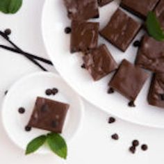 pieces of chocolate sitting on top of a white plate next to green leaves and beans