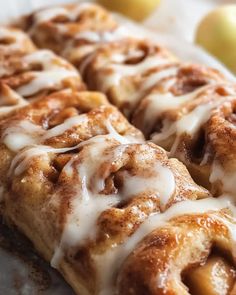 cinnamon rolls with icing sitting on top of a white plate next to an apple