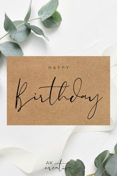 a card with the words happy birthday written on it next to eucalyptus leaves and paper