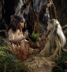 two women dressed in fairy costumes standing next to each other with trees and plants behind them