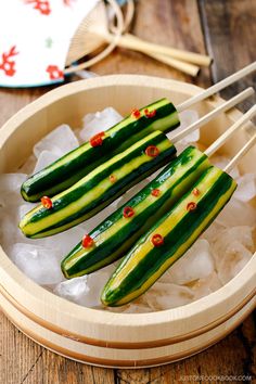 cucumber sticks are sitting on ice in a wooden bowl with chopsticks