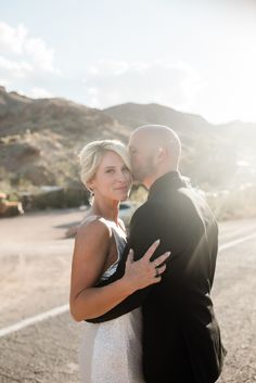 a bride and groom standing in the middle of an empty road with mountains in the background