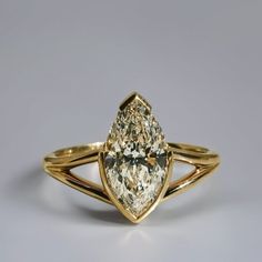 a yellow gold ring with a pear shaped diamond on it's side, set against a gray background