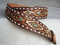 a pair of brown and green leather belts on a white cloth covered surface with an intricate design