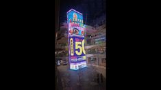 an illuminated sign in the middle of a shopping mall with people walking around it at night