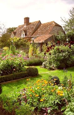 the garden is full of colorful flowers and plants in front of an old brick house