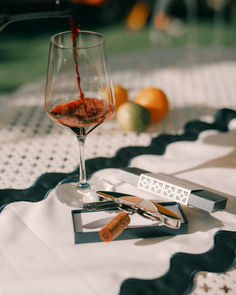 A close-up of a wine glass being poured, paired with a scalloped table runner and holiday-inspired decor—perfect for festive gatherings. Keywords: holiday tablescape, wine and dining, scalloped decor, al fresco entertaining, festive hosting. Bottle Opener, Vibrant Colors, Gift Wrapping, Stainless Steel, Gifts