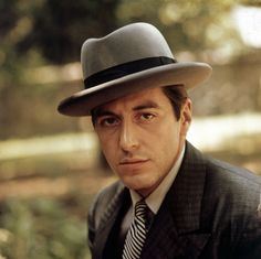 a man wearing a suit and tie with a hat on top of his head is looking at the camera