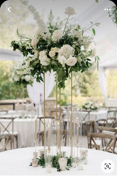 tall vases filled with white flowers and greenery on top of a round table