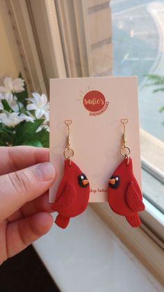 a pair of red bird shaped earrings sitting on top of a white card next to a window