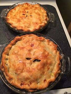 two pies sitting on top of an oven next to each other in pans