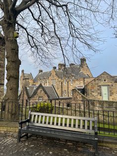 a wooden bench sitting next to a tree in front of a large stone building on a cloudy day