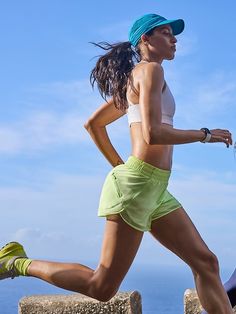 a woman is running on the beach in shorts and a hat with her hair blowing back