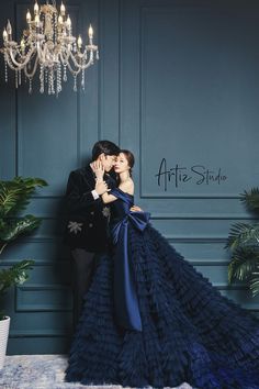 a man and woman are kissing in front of a wall with chandelier hanging from it