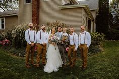 a group of people standing in front of a house with flowers on the grass and one person holding a bouquet