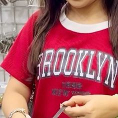 a woman cutting food with a pair of scissors in front of her face and wearing a red t - shirt that says brooklyn