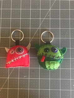 two keychains made to look like they are wearing halloween costumes, one is green and the other is red