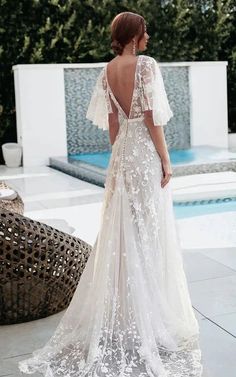 a woman standing in front of a pool wearing a wedding dress with sheer sleeves and open back