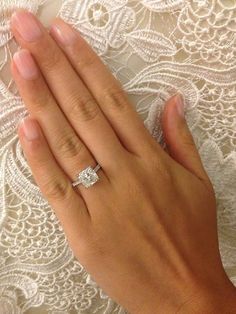 a woman's hand holding an engagement ring on top of a lace tablecloth