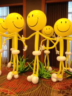 three yellow balloons with faces and arms are standing in the middle of a carpeted room