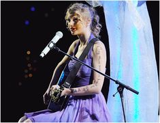 a woman in a purple dress is holding a guitar and singing into a microphone on stage