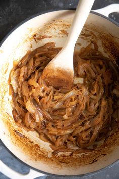 the food is being cooked in the pot with a wooden spoon on top and brown sauce