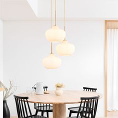 a dining room table with four chairs and three lights hanging from it's ceiling