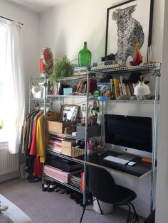 a computer desk sitting in front of a window next to a shelf filled with books