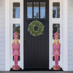 two pink nutcrackers are standing in front of a black door and wreath