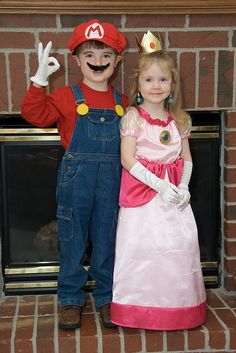 two children dressed up as mario and luigi in front of a fireplace with their hands on the hips