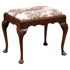 an ornate wooden bench with a floral upholstered seat cover on it's legs