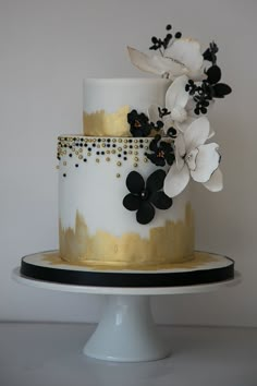 a white and gold wedding cake with black flowers on the top tier, sitting on a pedestal