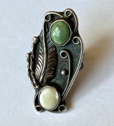 "an amazing and amazingly tall southwestern ring, artisan-made. top stone looks like a green turquoise, bottom one is a mother-of-pearl. beautiful feather and details, nice condition. marked with a stamping on the back. has a fair amount of patina but not much in the way of wear. mother-of-pearl shows some surface wear. size: 5.75 height of face: 1 and 15/16\" width of face: a bit over 13/16\" width of inner band: a bit over 1/16\"" Green Bohemian Multi-stone Rings, Bohemian Green Multi-stone Rings, Bohemian Multi-stone Opal Ring, Vintage Green Opal Ring, Unique Green Inlay Rings, Green Multi-stone Bohemian Jewelry, Green Bohemian Jewelry With Inlay, Bohemian Green Jewelry With Inlay, Bohemian Green Inlay Jewelry