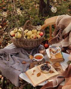 a picnic table with apples, cookies and tea on it in the fall leaves under a tree