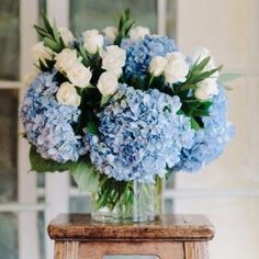 a vase filled with blue and white flowers on top of a wooden table next to a window