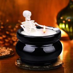 a lit candle with a skeleton on it sitting in a black bowl next to coins