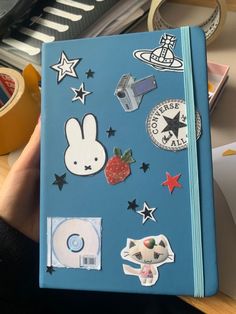 a hand holding a blue notebook with various stickers on it