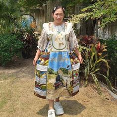 a woman standing in front of some plants and trees wearing a dress with pictures on it