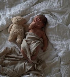 a baby laying on top of a bed next to a teddy bear with its eyes closed