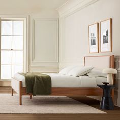 a bed with white sheets and pillows in a room next to two pictures on the wall